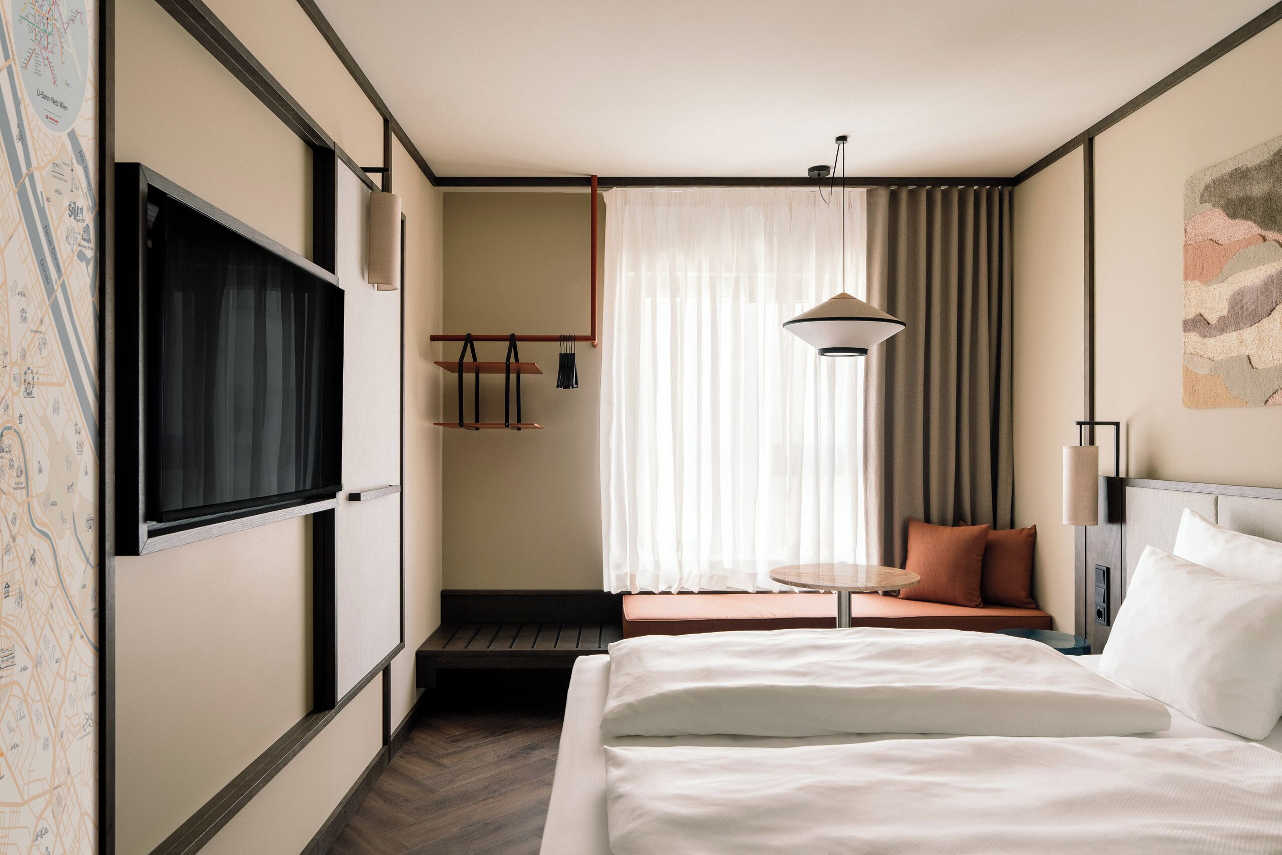 Habitación de hotel con cama, televisor, mapa en la pared, ventana con cortinas y una pequeña mesa con lámpara.