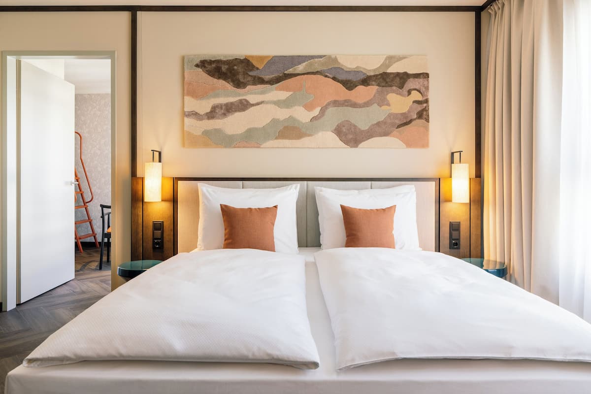 A double bed with white and brown pillows, two wall-mounted lamps, and a large abstract painting above the bed.