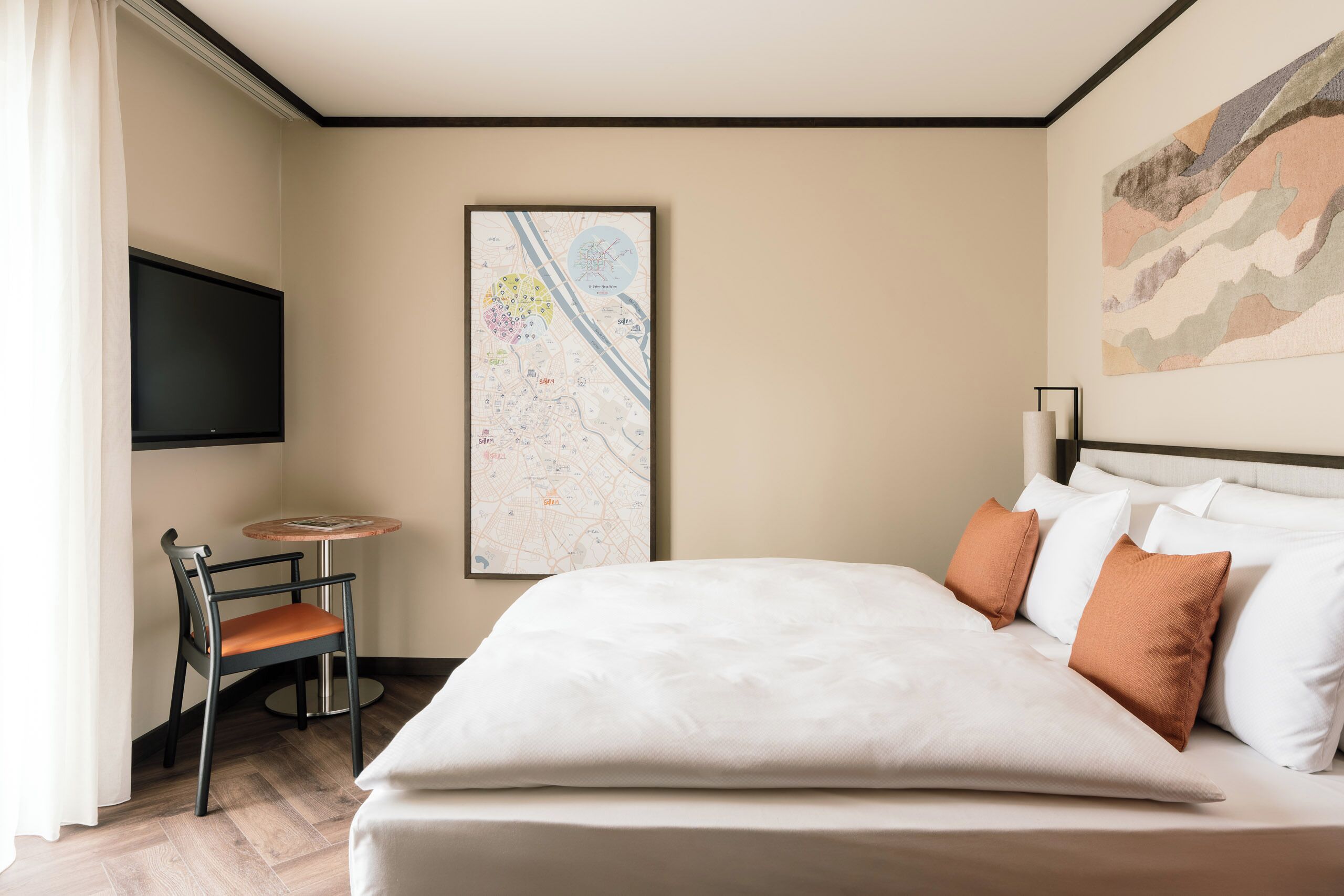 A hotel room with a bed, a chair, a TV, a map on the wall, and a painting.
