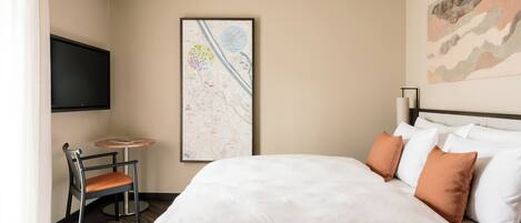 A hotel room with a bed, a chair, a TV, a map on the wall, and a painting.