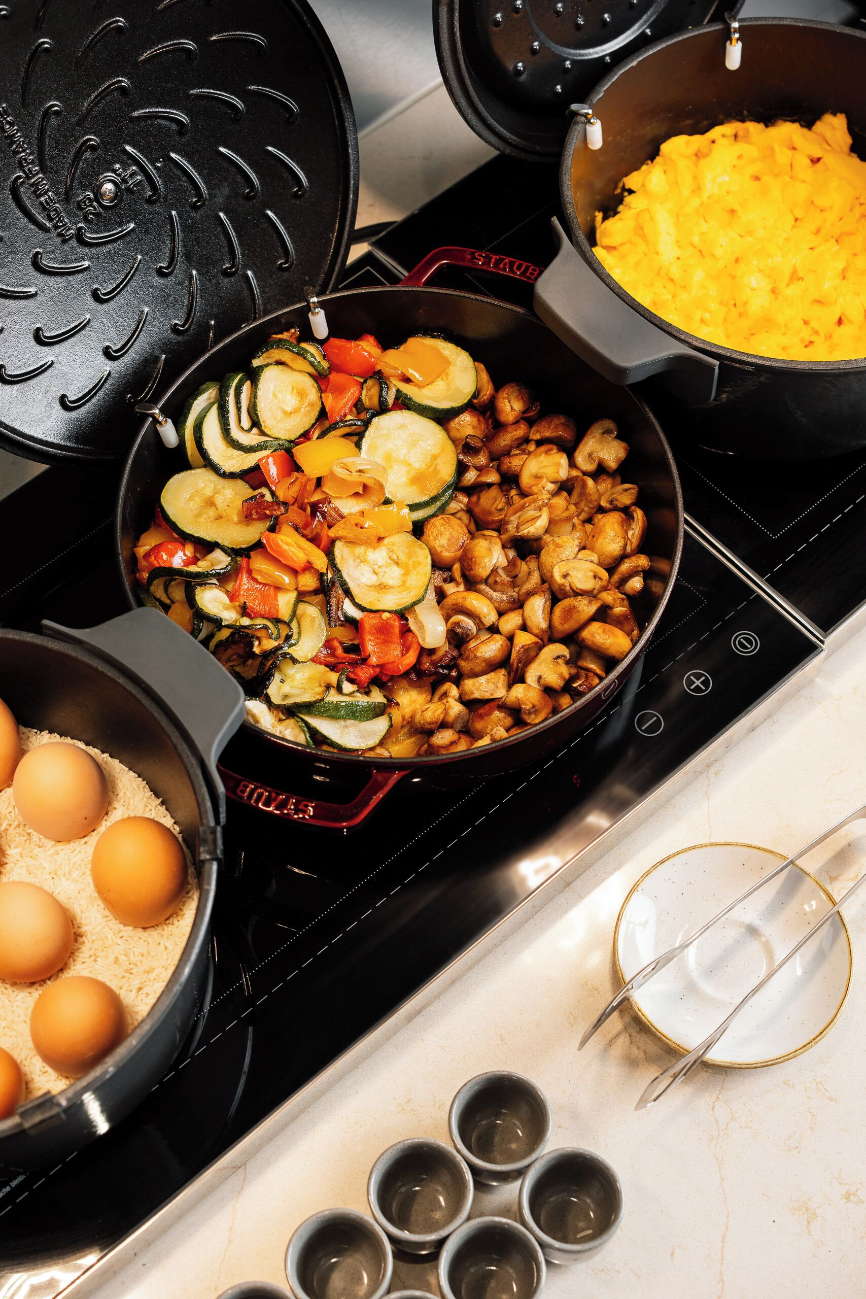 Una cocina con una olla de verduras, una sartén con huevos y un tazón de arroz.