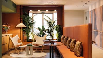Un interior moderno con piso de madera, una mesa redonda, un sofá con cojines y plantas en macetas.