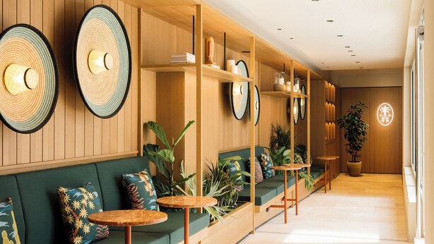 A modern interior with wooden paneling, green seating, and round tables.