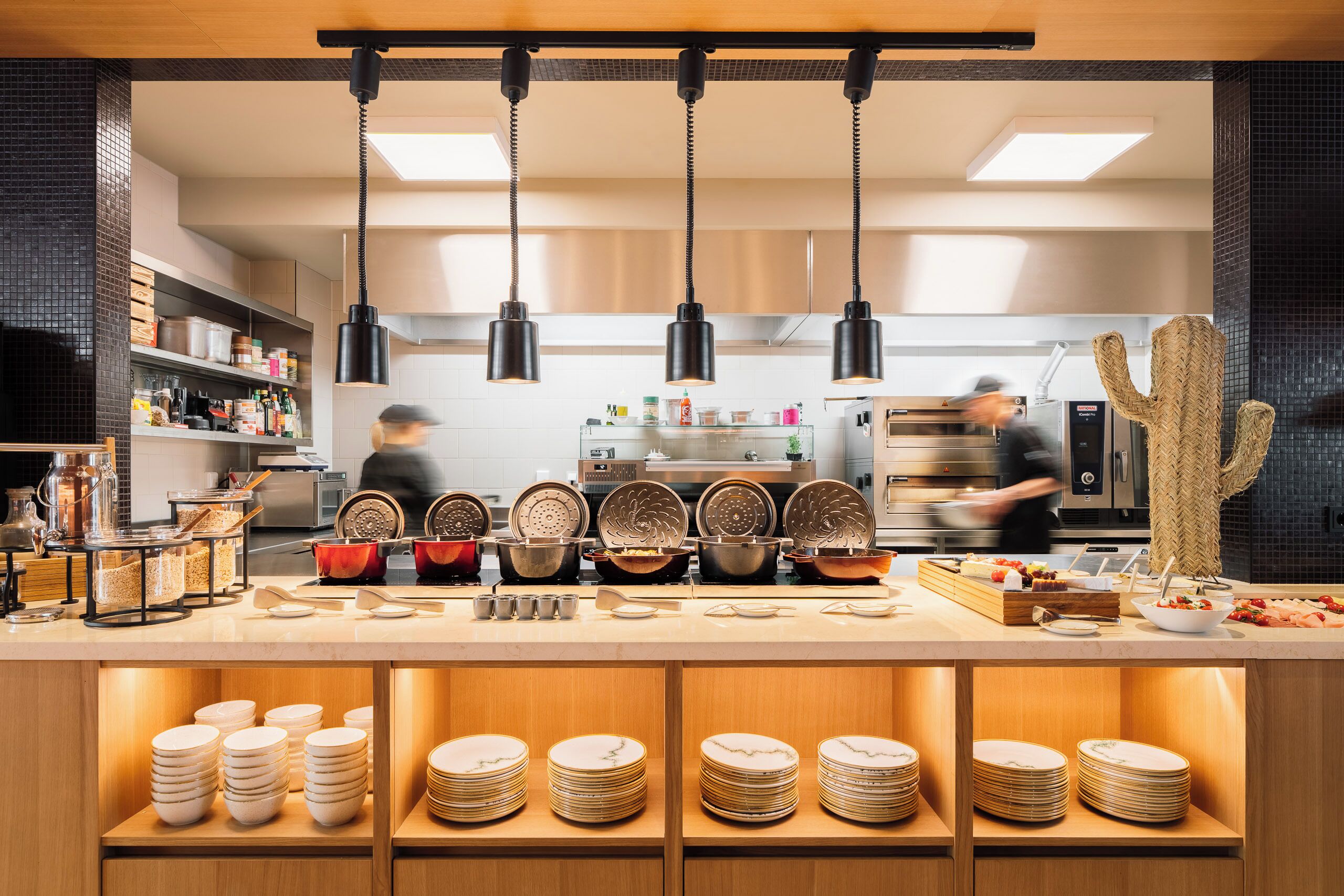 A modern kitchen with hanging pendant lights, a central island with various kitchenware, and a cactus decoration.