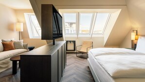 A modern hotel room with a bed, a desk, a chair, and a TV.