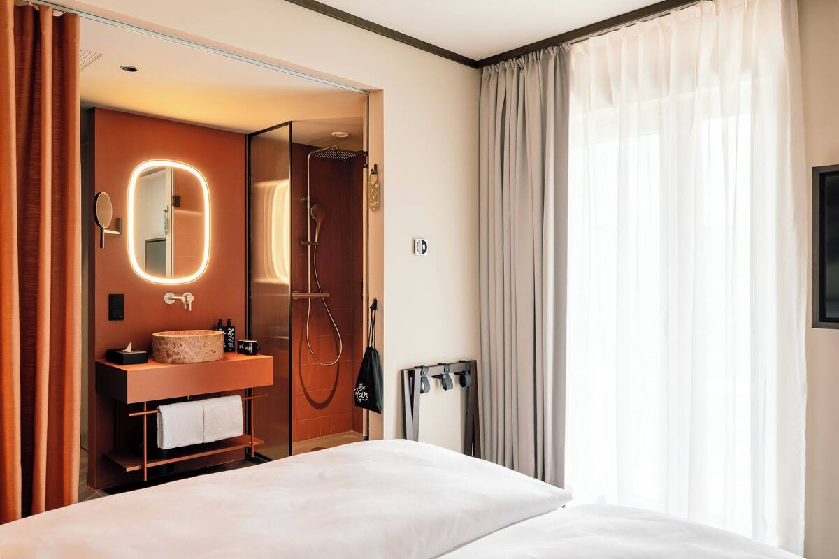 A hotel room with a bed, a bathroom with a mirror, a sink, and a shower.