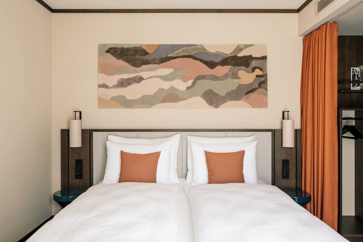 A hotel room with a bed, two bedside tables, a wall-mounted artwork, and a curtain.