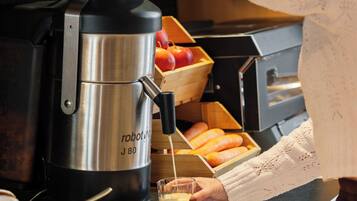 Una persona usando una máquina de café, con una bandeja de comida y una cesta de frutas al fondo.