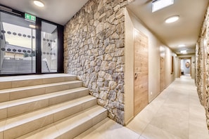 Un pasillo de hotel con paredes de piedra, puertas de madera y una escalera que sube a un nivel superior.