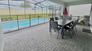 En overdækket terrasse med pool, et bord med stole og en ventilator i loftet.