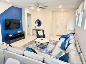 A modern living room with a grey sofa, a coffee table, and a TV mounted on the wall. - The Lovely Retreat near Disney w/ pool ! (Four Corners)