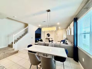 A spacious living area with a dining table, chairs, a sofa, and a staircase. - The Lovely Retreat near Disney w/ pool ! (Four Corners)