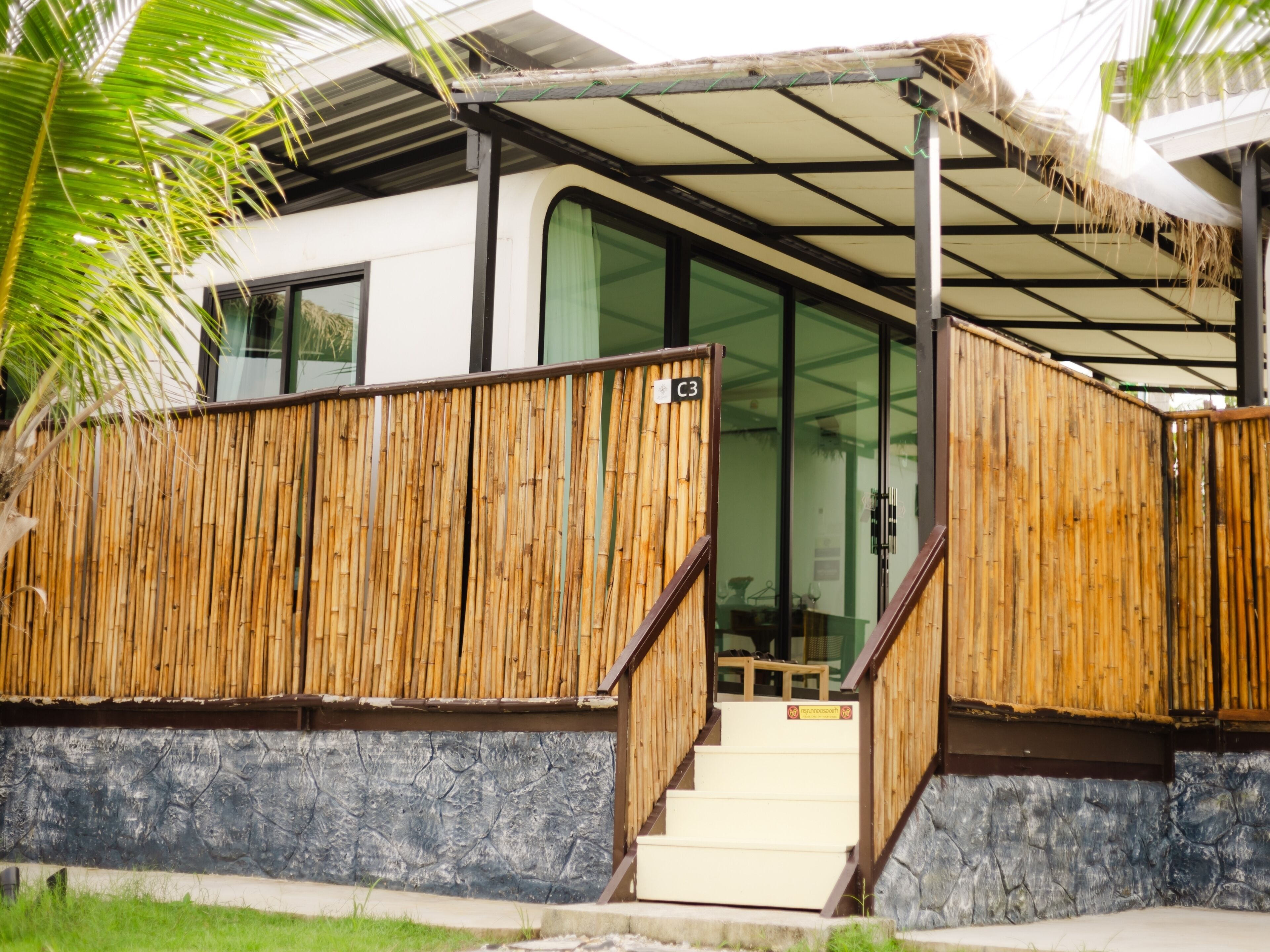 A modern building with a bamboo fence, a covered entrance, and a staircase leading to the main entrance.