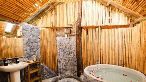 Een traditionele Japanse badkamer met een stenen muur, een houten badkuip en een stenen wastafel.