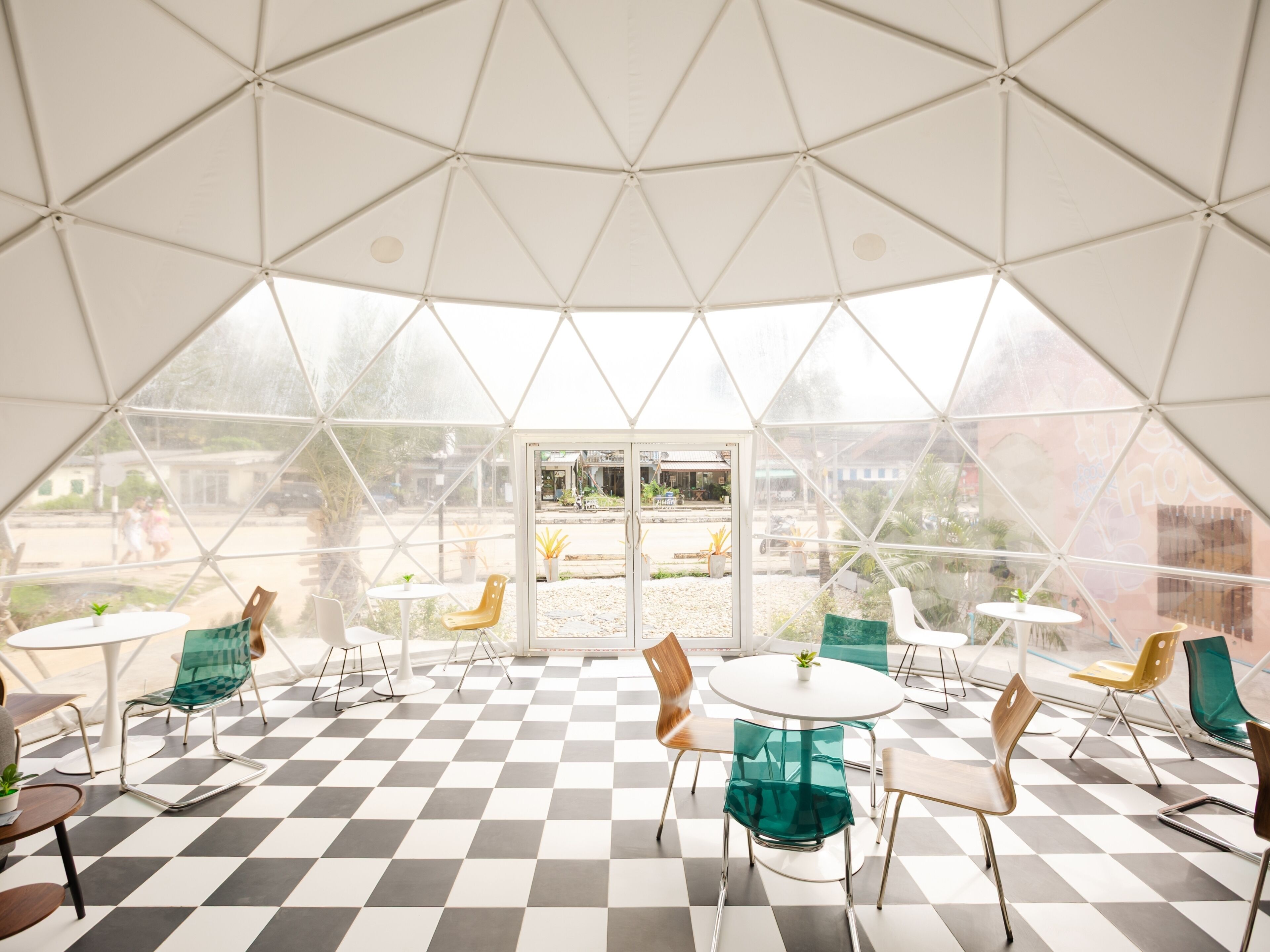 A spacious, geometrically designed interior with checkered flooring, multiple seating areas, and large glass windows offering views of the outside.
