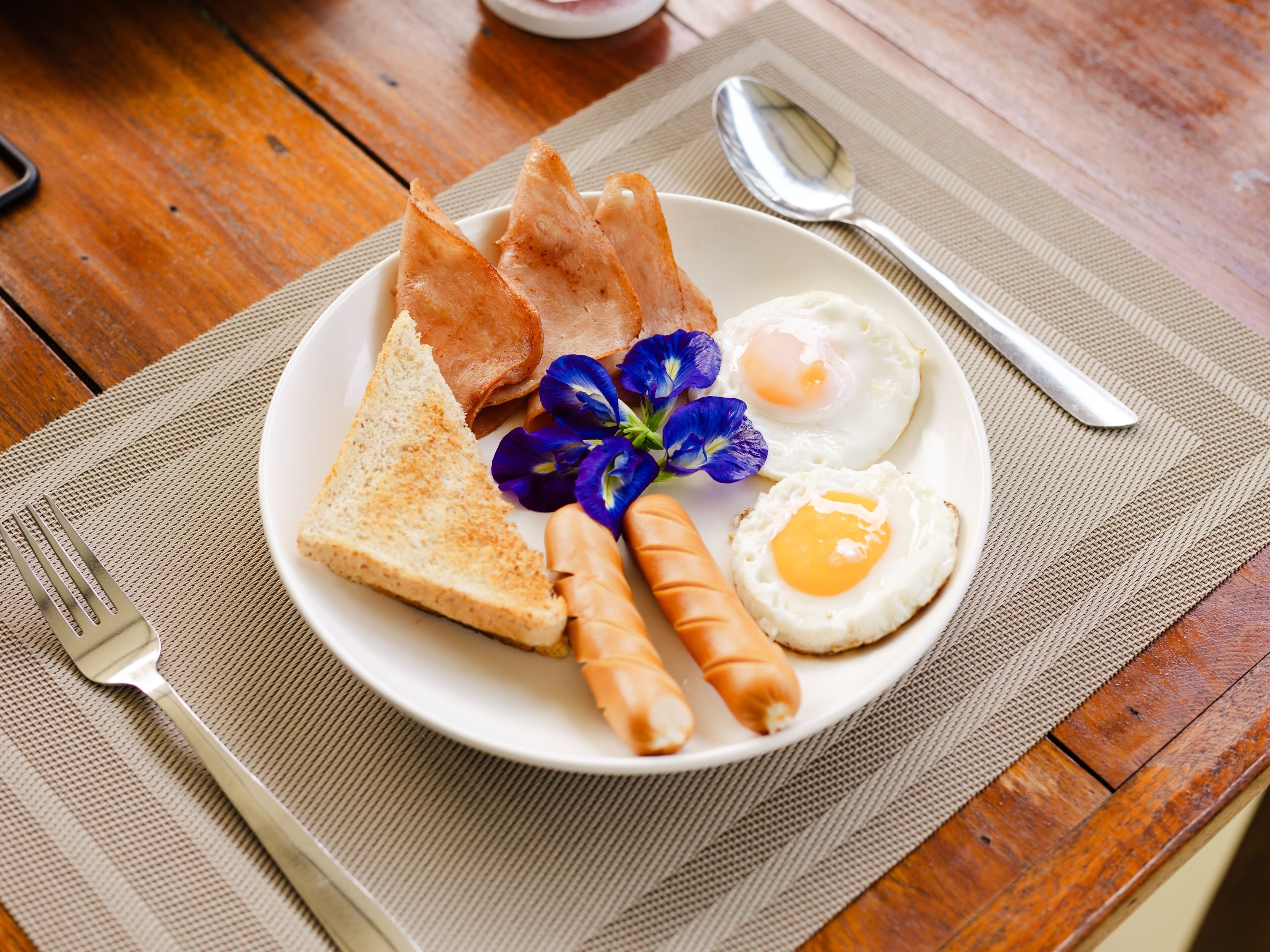 Une assiette de nourriture pour le petit-déjeuner comprenant des toasts, des saucisses, des œufs au plat et une petite fleur.