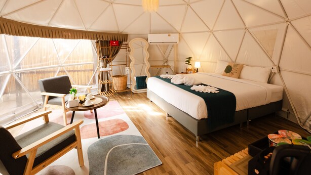 Een tent-achtig vertrek met een bed, een stoel, een tafel en een hanglamp.