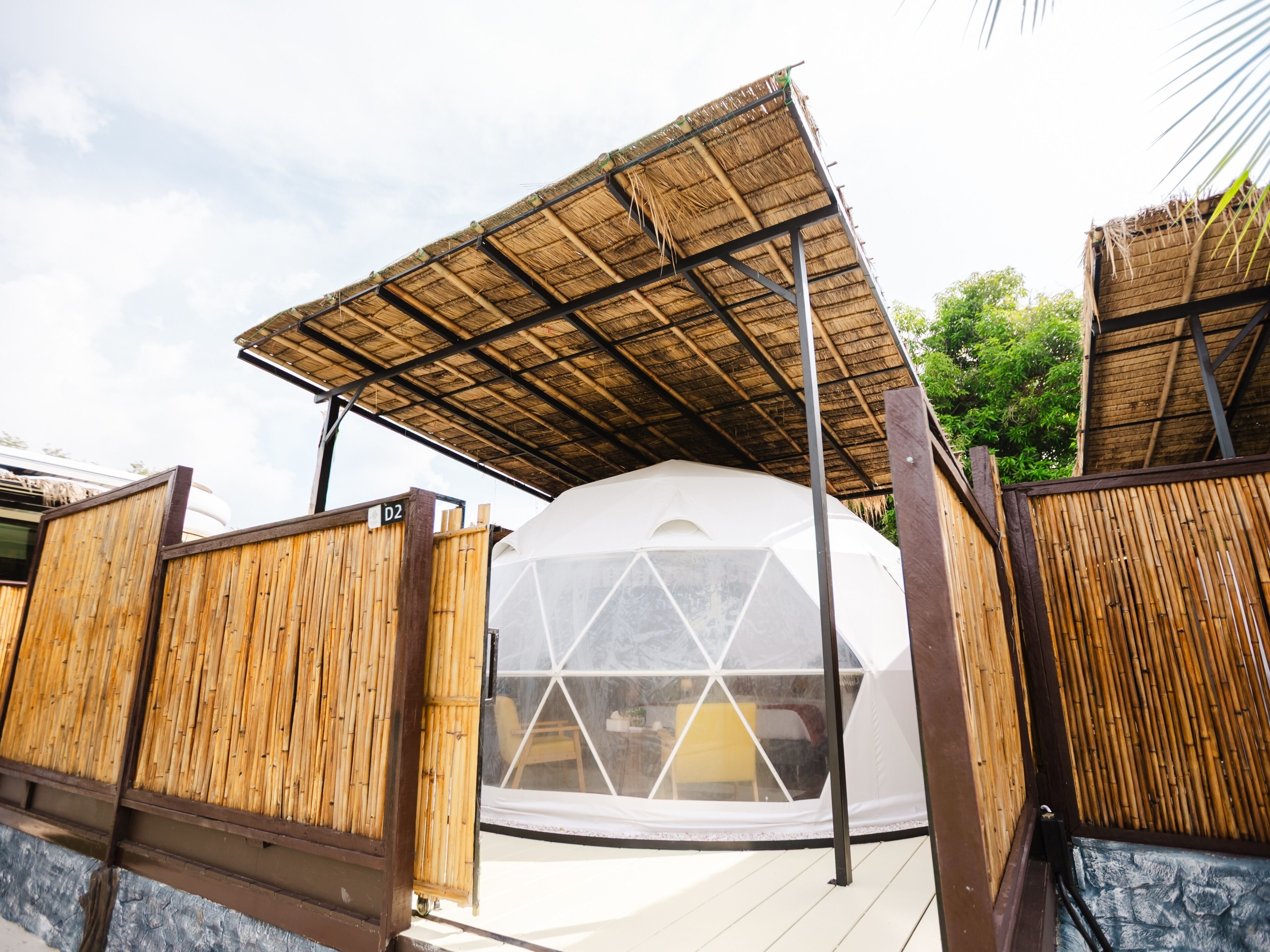 A geodesic dome structure with a bamboo fence and a thatched roof.
