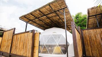 A geodesic dome structure with a bamboo fence and a thatched roof.