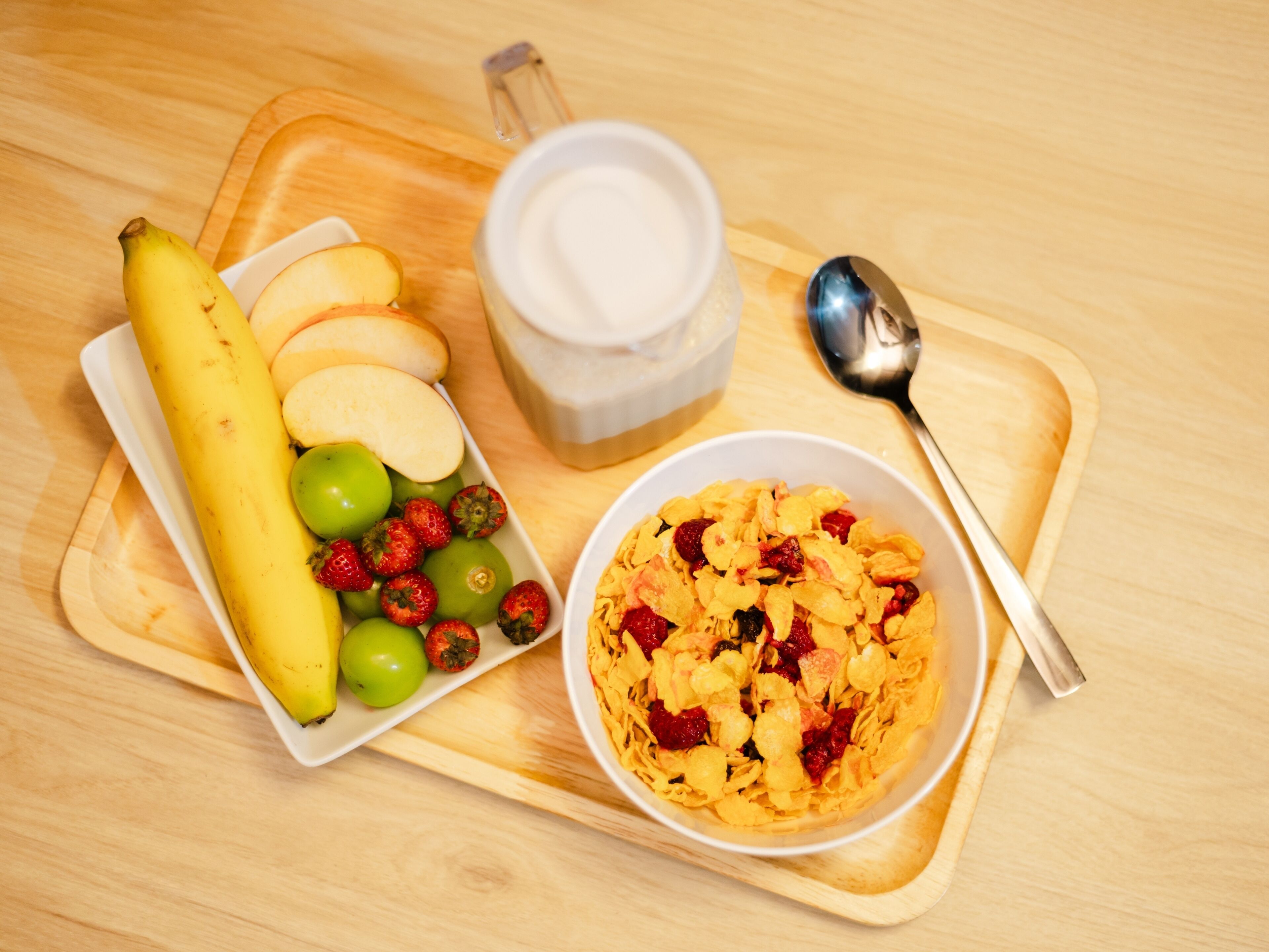 A tray with a banana, sliced apples, strawberries, and a bowl of cereal with dried fruits.