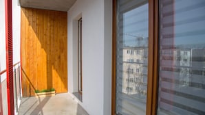 A narrow corridor with a wooden door, a window with a view of buildings, and a small planter with plants. - AS HOME Kosciuszki (Wrocław)