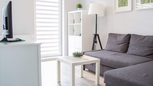 A modern living room with a grey sofa, a white coffee table, a standing lamp, and a TV on a white cabinet. - AS HOME Kosciuszki (Wrocław)