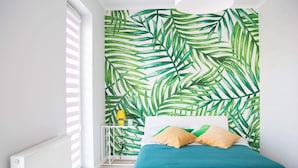 A bedroom with a large window, a bed with teal bedding, and a wall with a green leaf pattern. - AS HOME Kosciuszki (Wrocław)