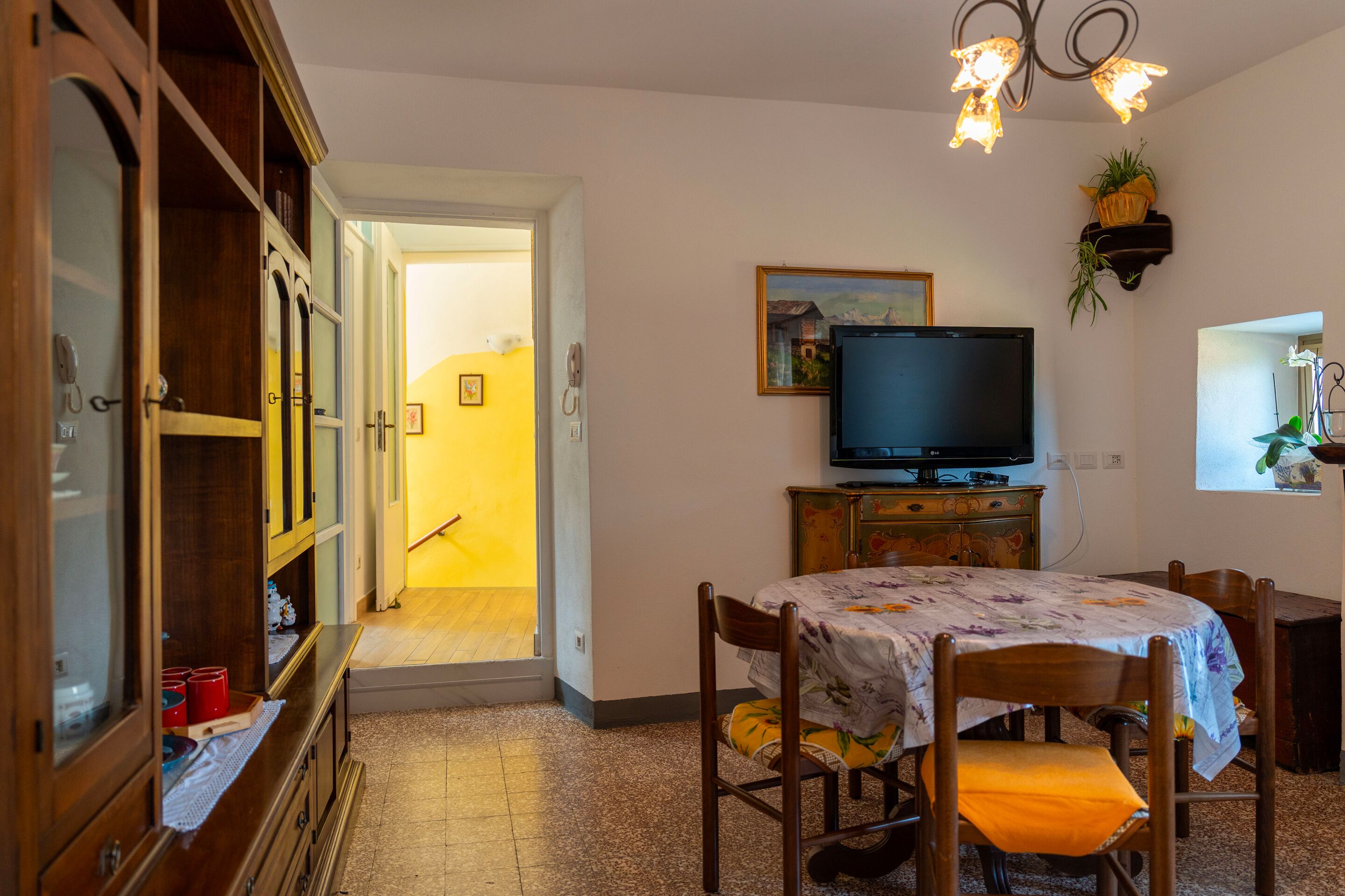 A dining area with a table set for two, a television, and a cabinet with glass doors.