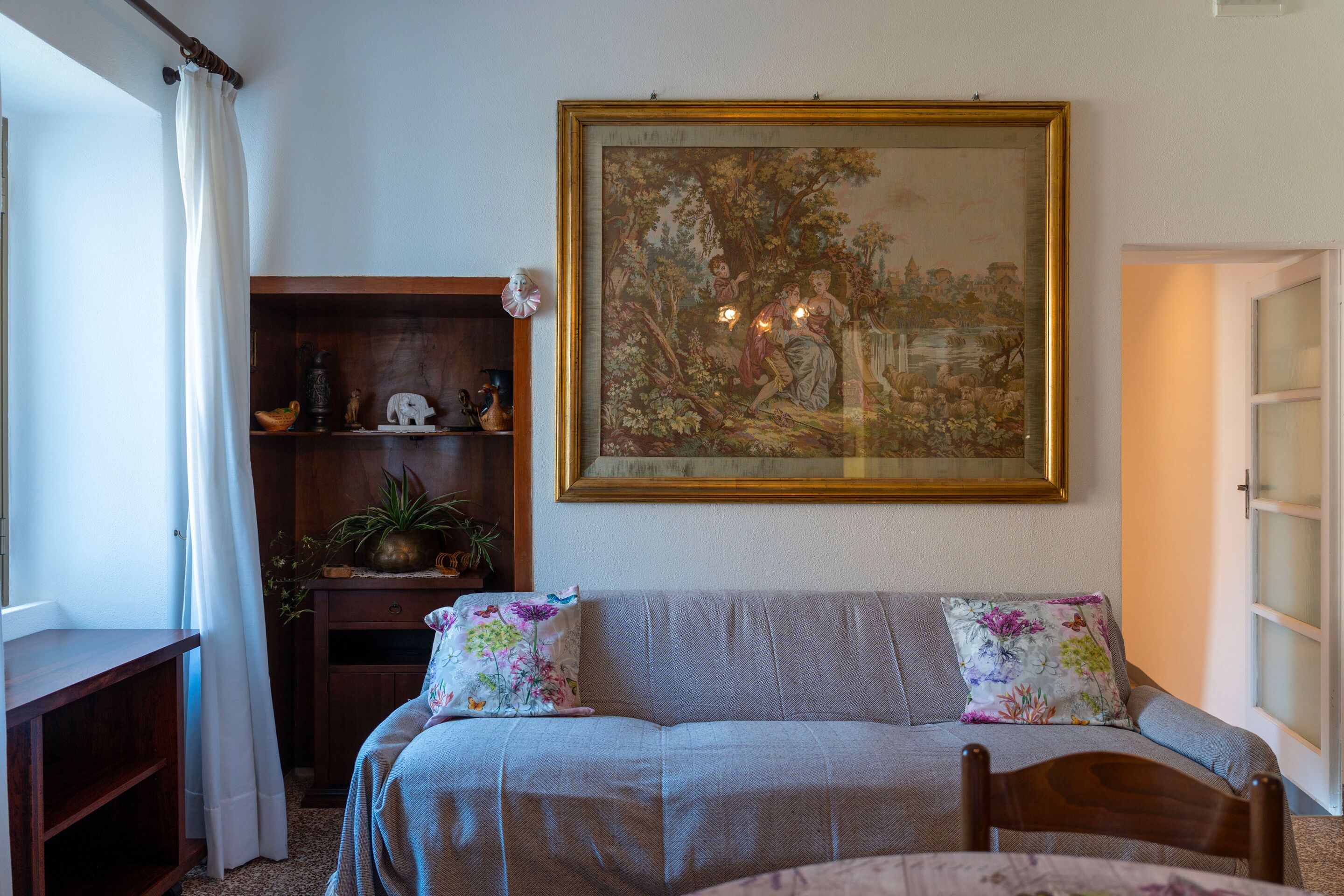 Una habitación con cama, un armario de madera, un cuadro y una ventana con cortinas.