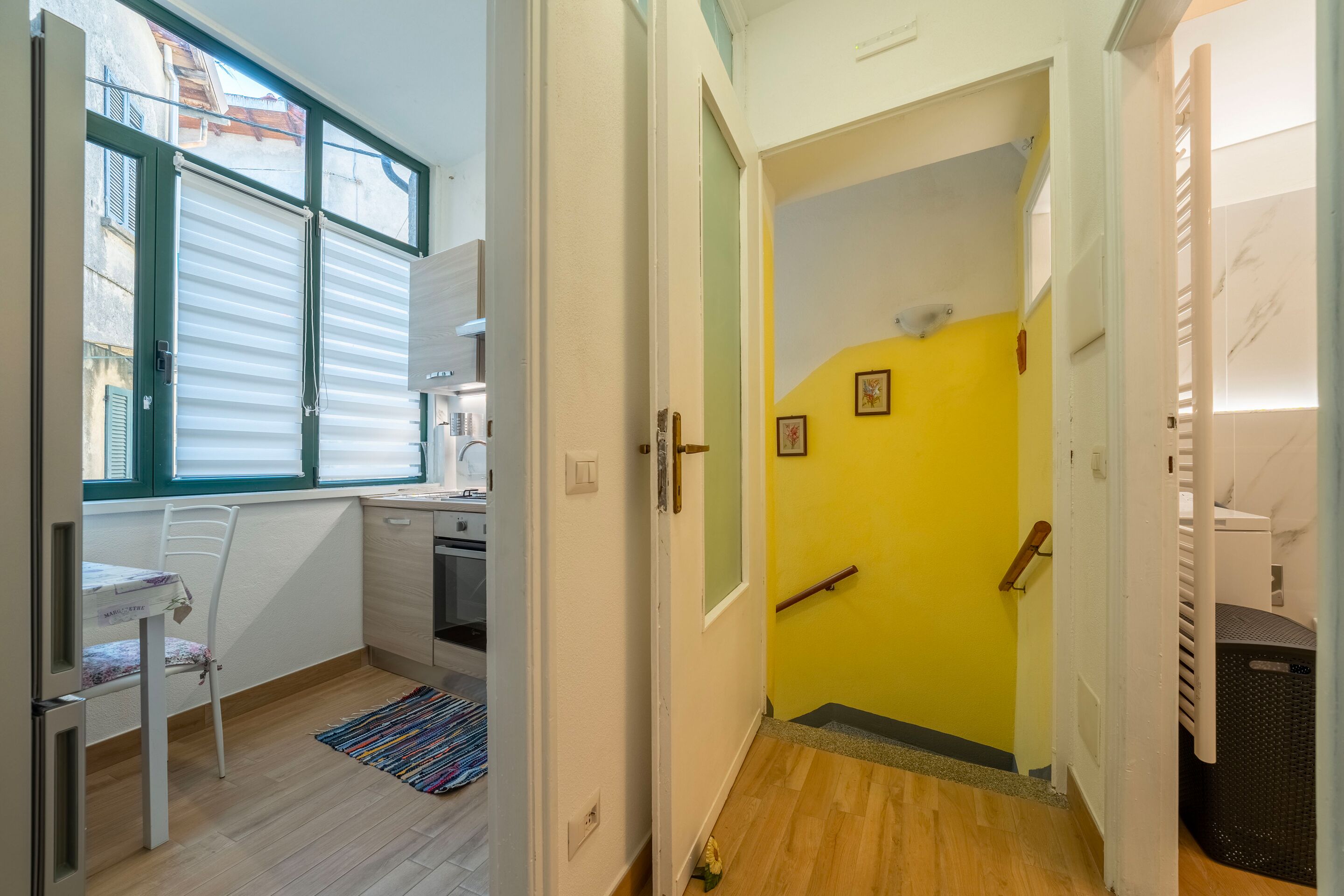 Eine kleine Küche mit Essbereich, eine Treppe zu einem raumgelb gestrichenen Zimmer und einem Wäschekorb.
