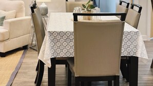 Un comedor con una mesa dispuesta para cuatro personas, rodeada de sillas, una lámpara y un florero con flores.