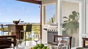 A dining area with a table set for two, a grill, and a view of the ocean. - Urunga Magic – A beautiful waterfront retreat in Urunga with serene river and ocean views (Urunga)