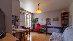A cozy living room with a wooden dining table, a red chair, a sofa, and a bookshelf.