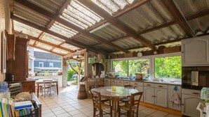 A kitchen with a tiled floor, wooden chairs, a round table, and a window with a view of greenery.