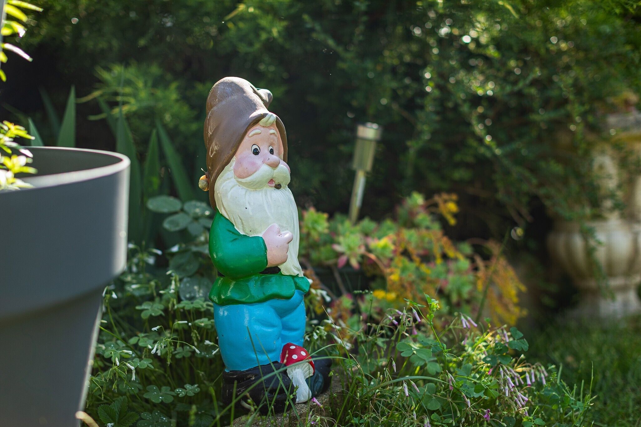 A garden statue of a bearded man in a green jacket and blue pants.