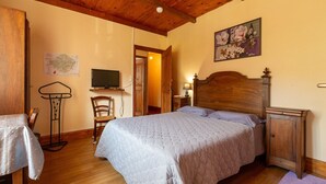 A bedroom with a wooden bed, a nightstand, a dresser, a chair, a map on the wall, and a television.