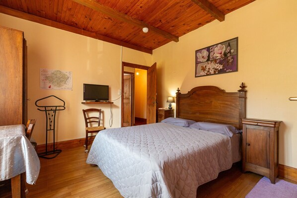 Une chambre à coucher avec un lit en bois, une table de chevet, une commode, une chaise, une carte accrochée au mur et un téléviseur.