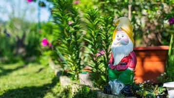 A garden statue of a gnome with a beard, wearing a red jacket and green pants, sitting on a stone.