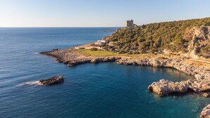 Eine Küstenlandschaft mit einer Burg auf einem Hügel, felsiger Küste und klarem, blauem Meer.