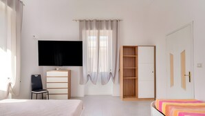 Ein Schlafzimmer mit Bett, Fernseher, Stuhl, Kleiderschrank und Schreibtisch.