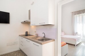 Een kleine keuken met een spoelbak, kookplaat en kastjes, een bed met raam, en een flatscreen televisie aan de muur bevestigd.