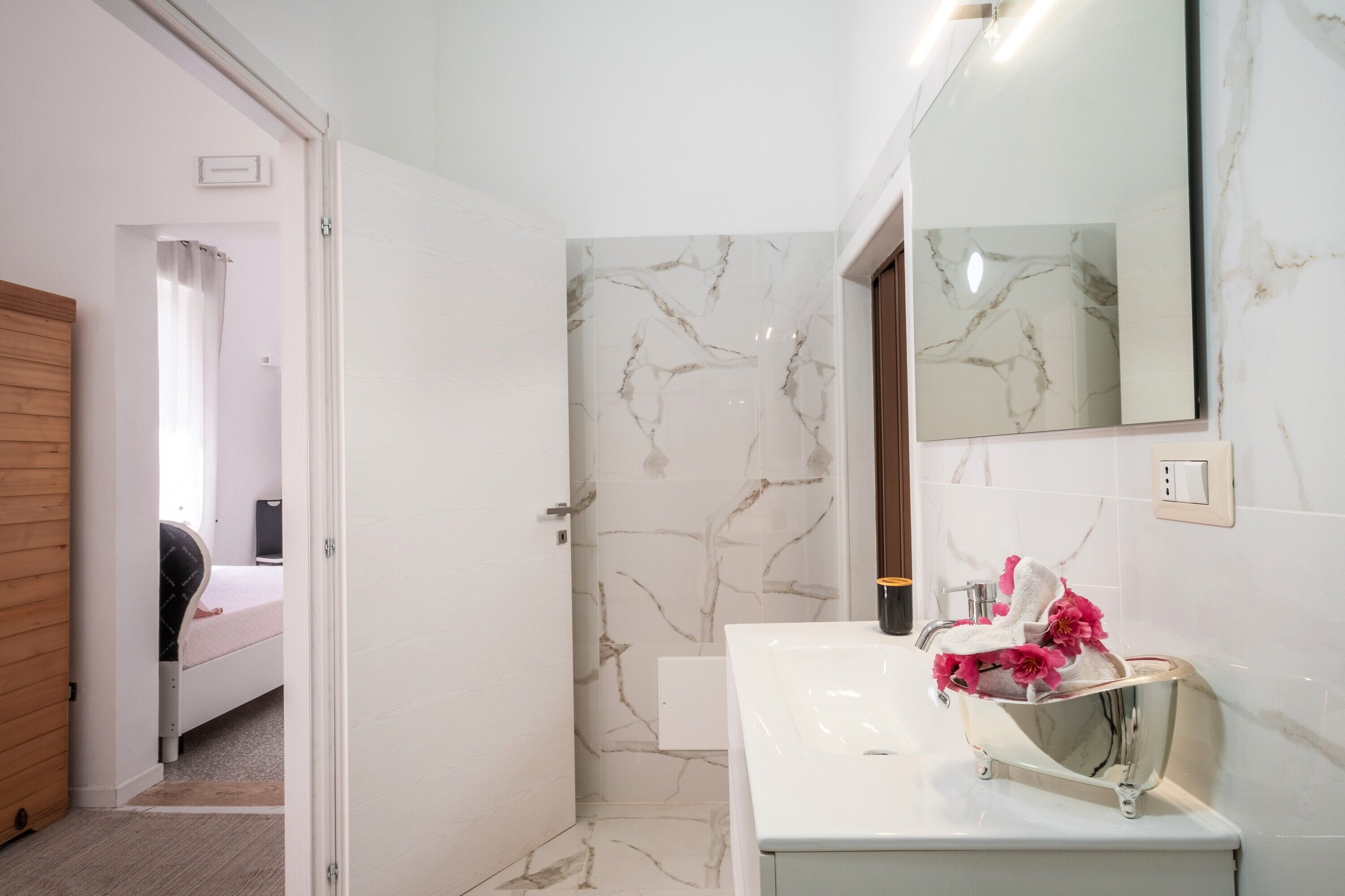 A modern bathroom with a white sink, a mirror, and a shower area.