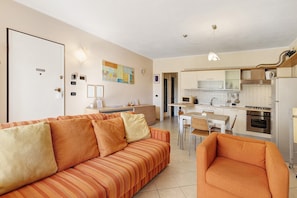 Un espacio habitable compacto con sofá, una silla, kitchenette y comedor.