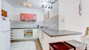 Una cocina con armarios blancos, un armario superior rojo, encimera de granito, horno empotrado y lámpara colgante.