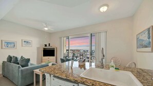 A modern kitchen with a granite countertop, white sink, and a dining area with a table and chairs. - Bay View Condo & Private Balcony | Pool & Hot Tub (St. Petersburg)