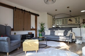 Una sala de estar moderna con un sofá gris, un otoman amarillo, una mesa de centro redonda y una planta grande.