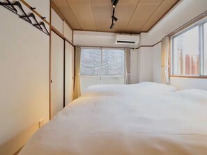 A bedroom with a large bed, a window with curtains, and an air conditioning unit. - CHITOSE CORPO (Tokyo)
