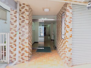 A hallway with patterned brick walls, a tiled floor, and a closed metal shutter on the right. - CHITOSE CORPO (Tokyo)