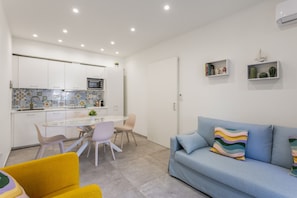 Una cocina moderna con armarios blancos, una mesa de comedor de vidrio y un sofá azul con cojines coloridos.