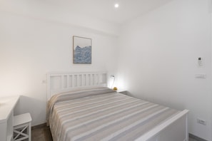 A bedroom with a bed, a bedside table, a lamp, and a wall-mounted light switch.